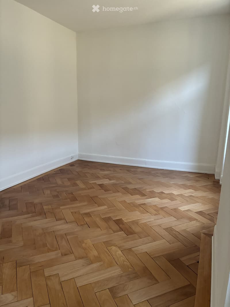 Empty room with light-colored walls and a herringbone-patterned wooden floor.
