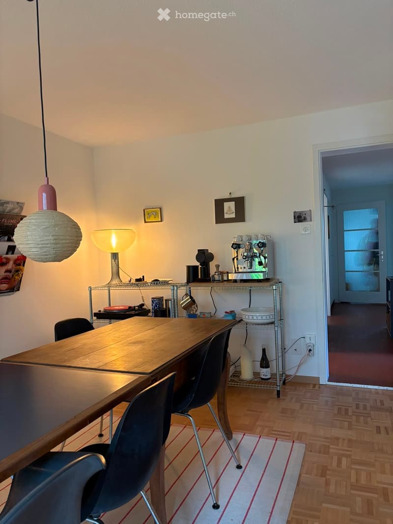 Modern kitchen with wooden table, black chairs, coffee machine, and decorative lamps.