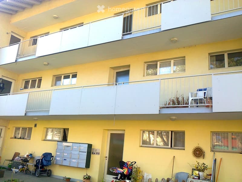 Multi-story residential building with yellow exterior, multiple balconies, windows, and outdoor seating areas.