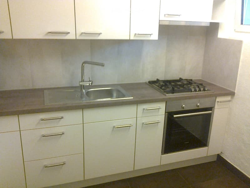 Modern kitchen with white cabinets, stainless steel sink, faucet, gas stove, and built-in oven.