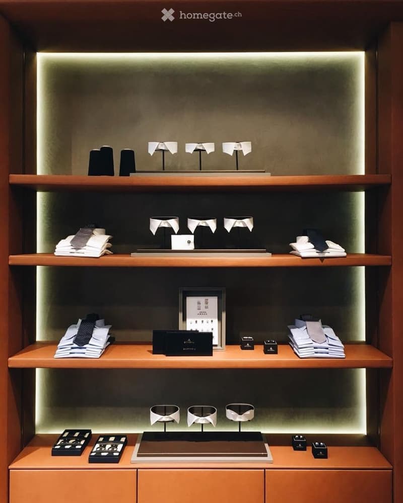 A neatly organized display area with wooden shelves holding folded ties, collar stays, and small boxes, illuminated by soft lighting.