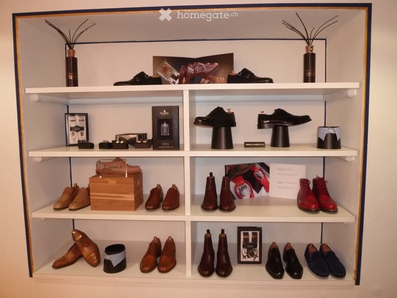 A neatly organized display cabinet filled with various pairs of shoes, decorative vases, framed pictures, and boxes, arranged on multiple white shelves.