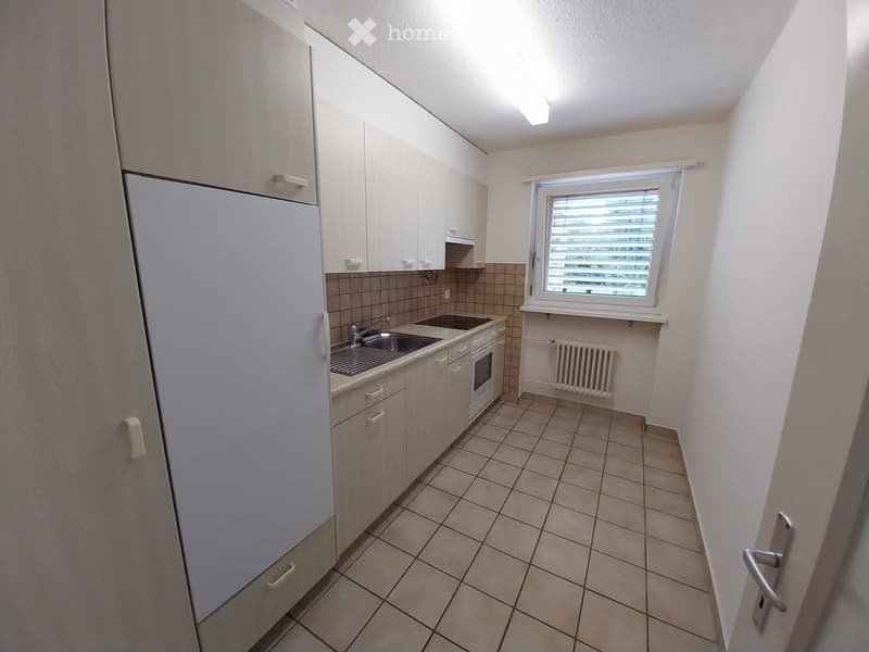 Modern kitchen with white cabinets, stainless steel sink, oven, refrigerator, and tiled floor.