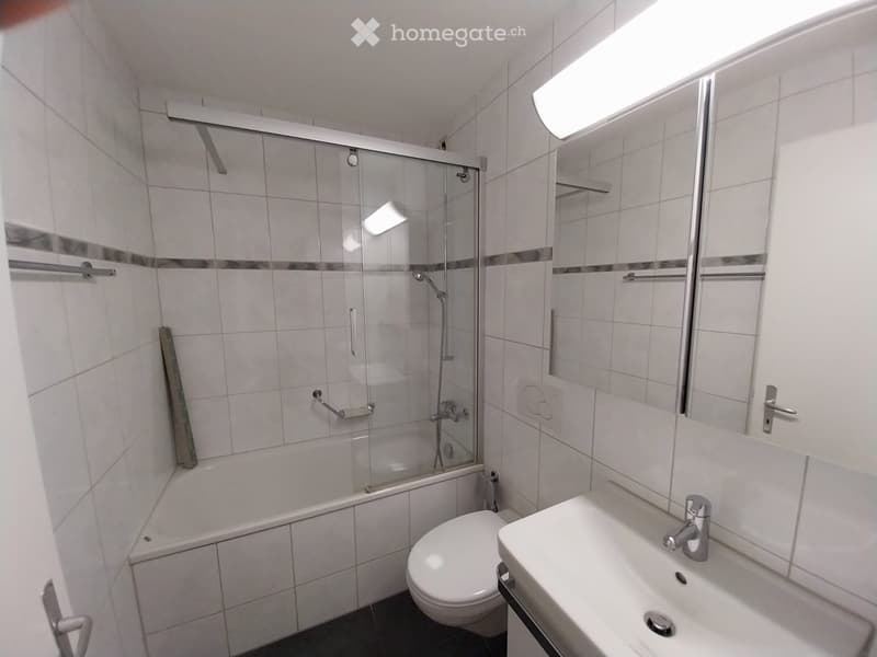 Modern bathroom with white tiles, a bathtub, toilet, sink, and a glass-enclosed shower area.