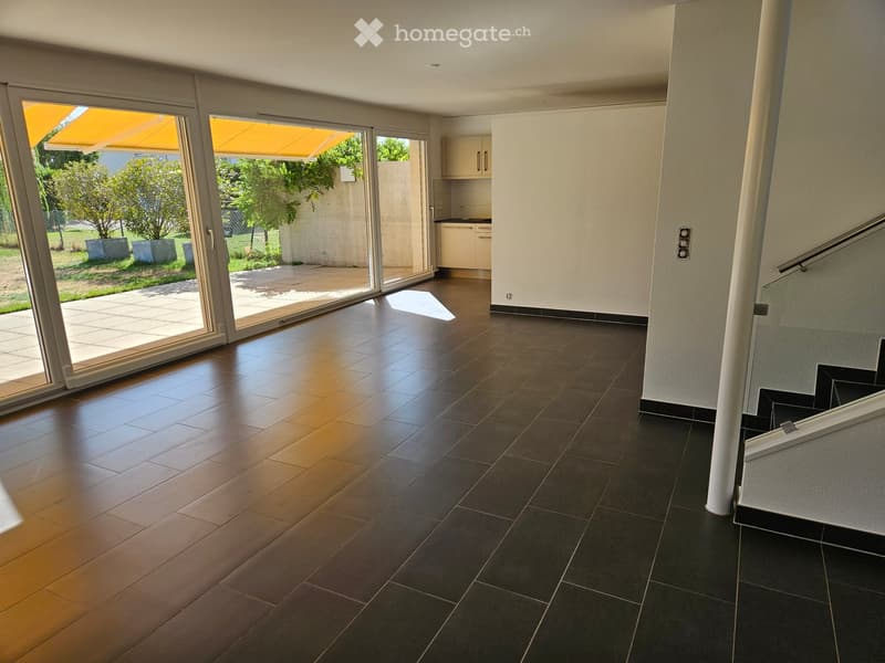 Empty room with dark tiled floor, light-colored walls, large sliding glass doors leading to a patio, and a small kitchen area with cabinets and a countertop.