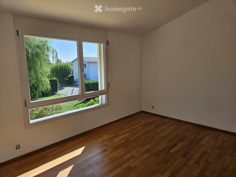 Empty room with wooden flooring and large windows offering a view of greenery outside.
