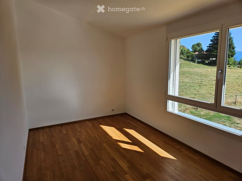 Empty room with wooden flooring and large windows offering a view of a grassy field and trees.