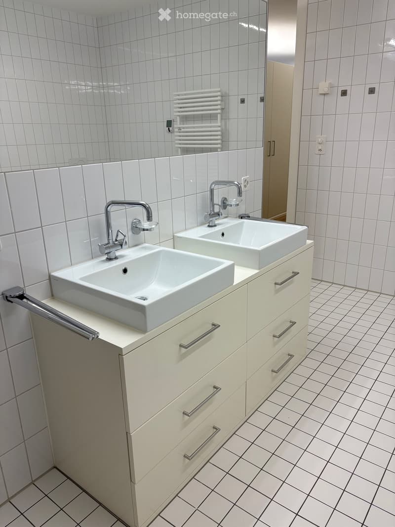 Modern bathroom with two white sinks, chrome faucets, and a white cabinet with silver handles.
