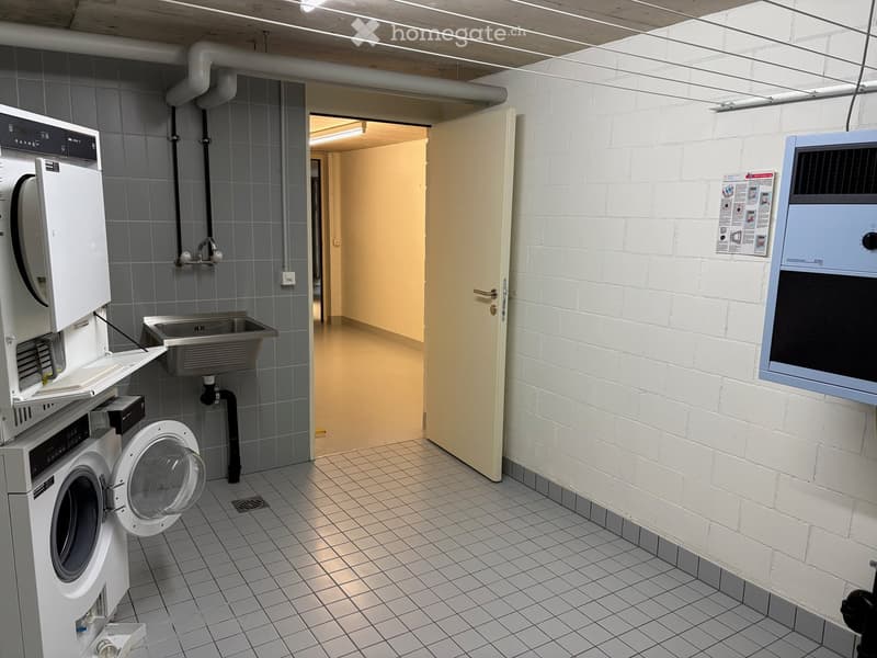Clean, modern bathroom with tiled floors and walls, featuring a washing machine, sink, and faucet.