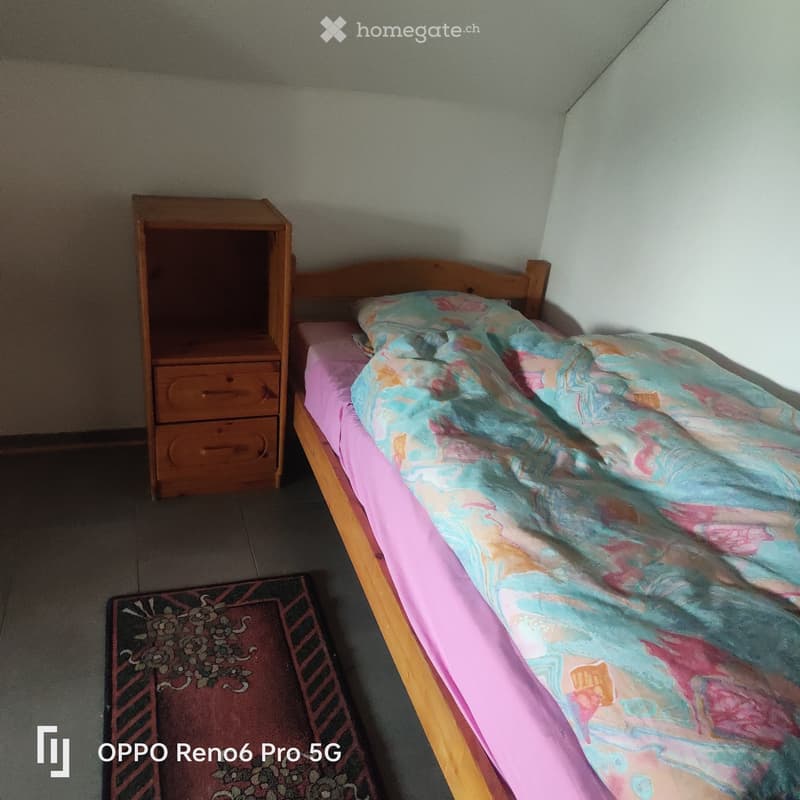A small bedroom with a single wooden bed, a nightstand, and a patterned rug on the floor.
