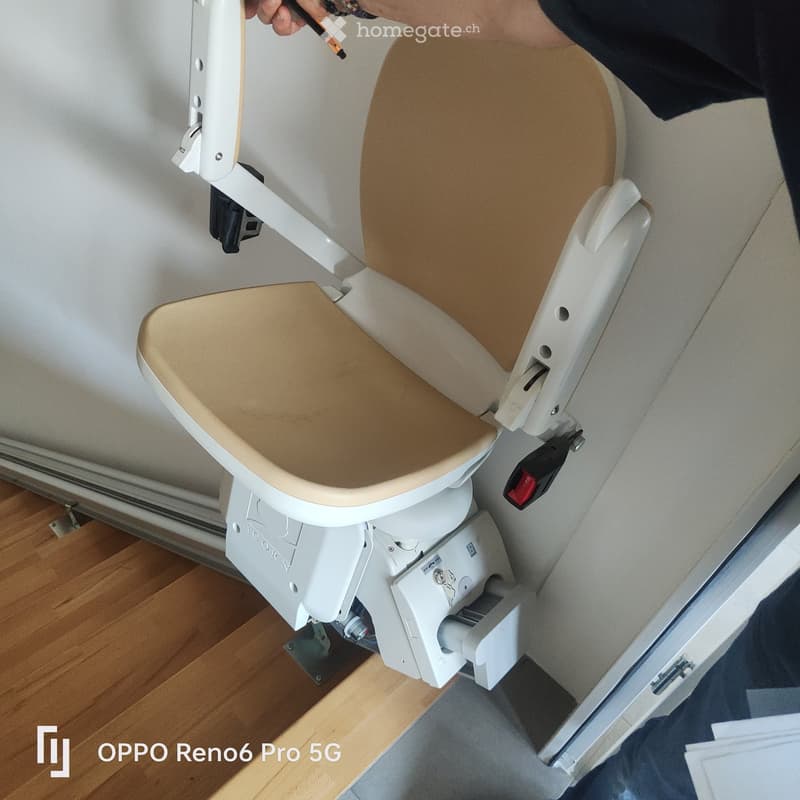 A beige upholstered chair with a white metal frame and adjustable backrest, mounted on a white base with mechanical components.
