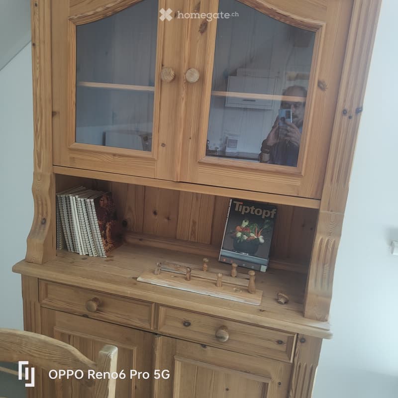 A wooden cabinet with glass doors and drawers, topped with a wooden desk surface holding books and a laptop.