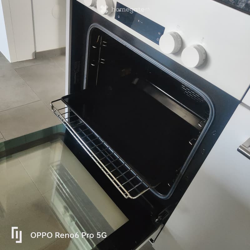 Modern built-in oven with open door, showing interior rack and control panel with knobs and digital display.