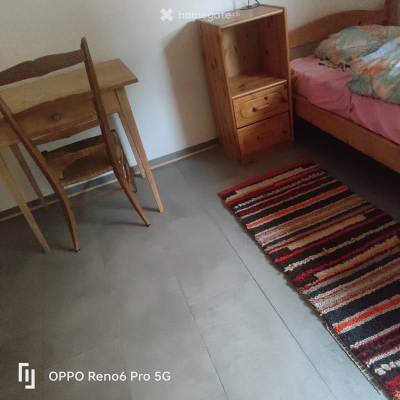 Bedroom with a wooden bed, nightstand, chair, and a colorful striped rug on the floor.
