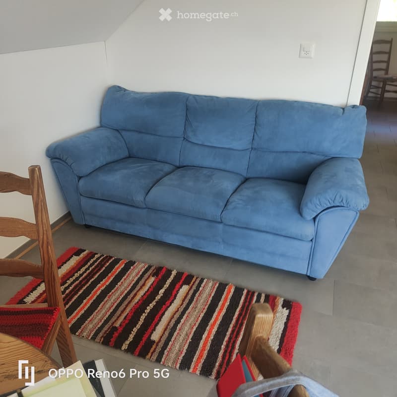 Living room with a blue sofa, wooden chair, and a striped rug on the floor.