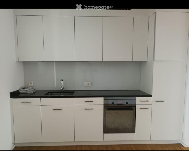 Modern kitchen with white cabinets, black countertops, a sink, and an oven. The space is clean and contemporary with a wooden floor.