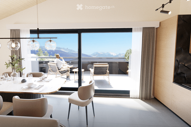 Modern dining area with a round wooden table, chairs, pendant lights, and a large window offering a scenic mountain view. A person is seated on the balcony outside.