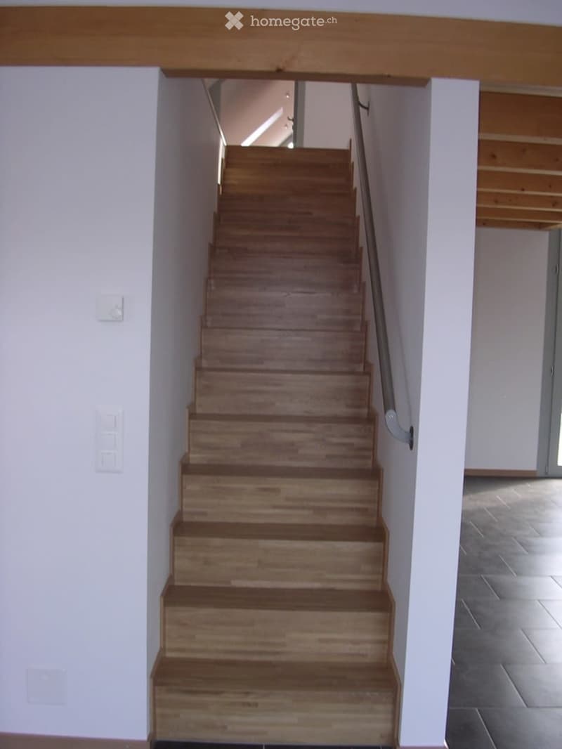 Wooden staircase with a metal handrail, white walls, and a tiled floor in a modern interior.