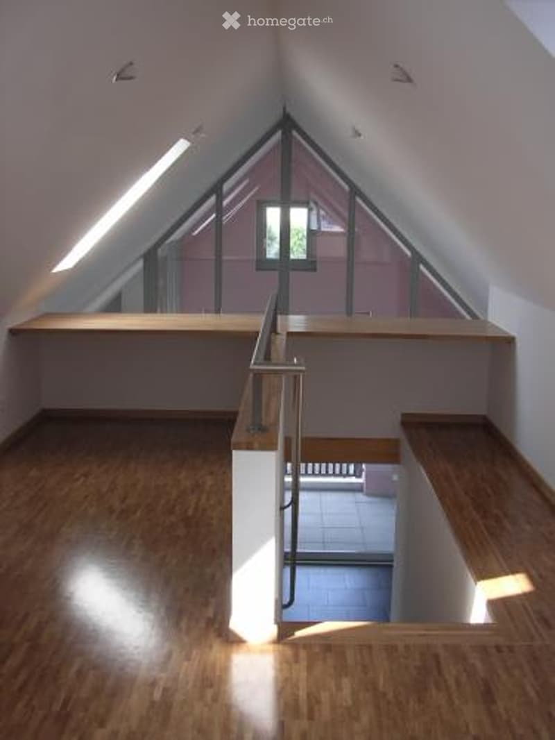 Attic space with wooden flooring, slanted ceilings, built-in wooden benches, and a metal railing leading to a lower level.