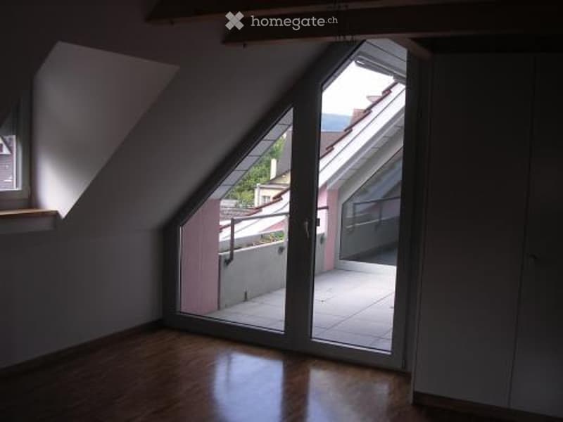 Bright, empty attic room with wooden flooring, large skylight windows, and access to a small balcony or terrace area.
