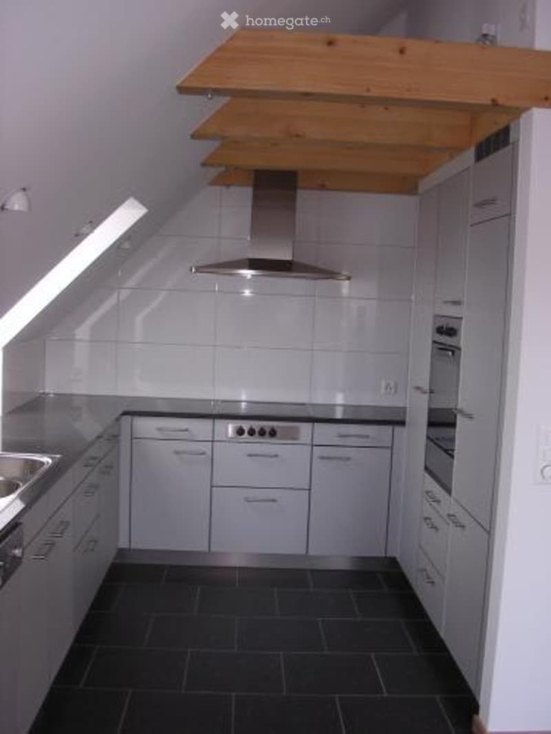 Modern kitchen with white tiled walls, stainless steel appliances, and dark tiled flooring.