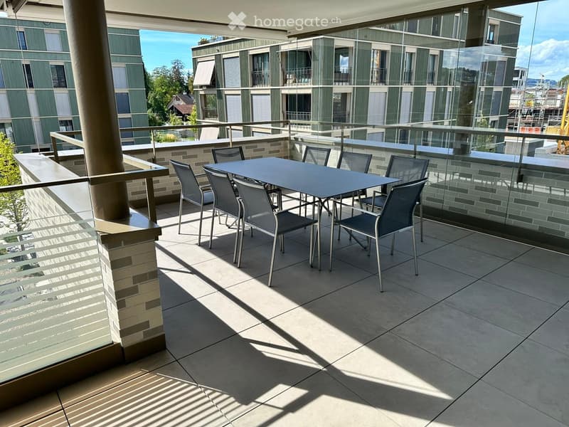 Balcony with a modern glass railing, tiled floor, and a dining set including a table and six chairs.
