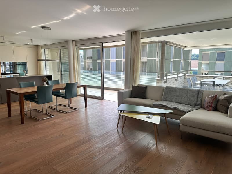 Modern living and dining area with hardwood floors, large windows, and a balcony. Features a grey sofa, coffee table, dining table, and chairs.