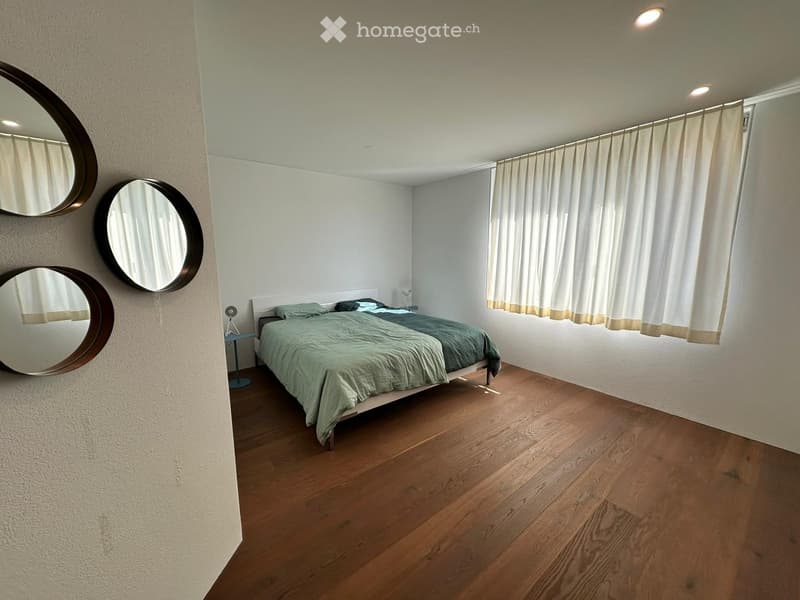 Modern bedroom with wooden flooring, a neatly made bed with green bedding, a nightstand, and three round wall-mounted mirrors.