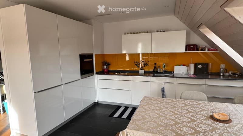 Modern kitchen with white cabinets, black countertops, and a yellow backsplash. Features a refrigerator, oven, sink, and a small dining area with a table and chairs.
