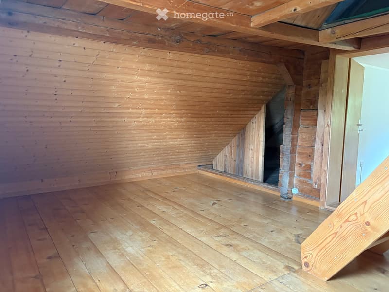 Empty attic space with wooden walls, ceiling beams, and floorboards. No furniture or equipment present.