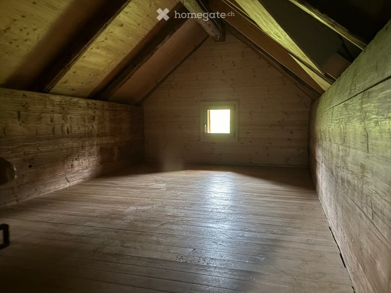 Empty attic space with wooden walls, floor, and a small window letting in light. No furniture or equipment present.