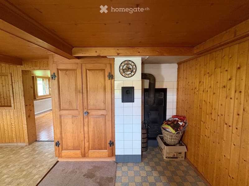 Cozy hallway with wooden walls, a tiled floor, a black wood-burning stove, a clock, and a wicker basket with items on a cardboard box.