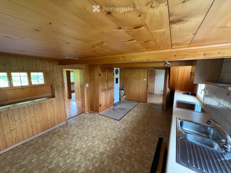 Bright kitchen with wooden walls and ceiling, featuring a stainless steel sink, countertop, and cabinets. The floor is made of cork tiles, and there are windows allowing natural light to enter.