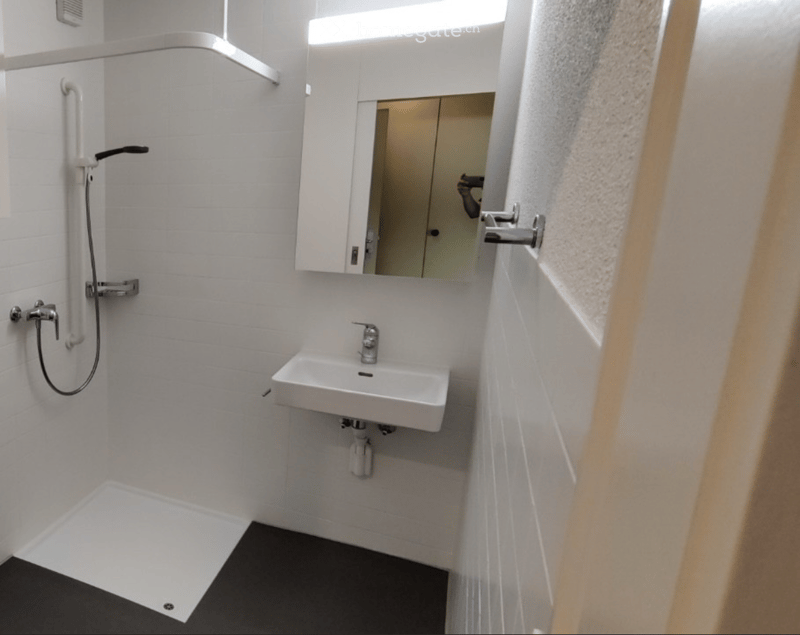 Modern bathroom with white tiled walls, a corner shower, a white sink with a modern faucet, and a mirrored cabinet above the sink.