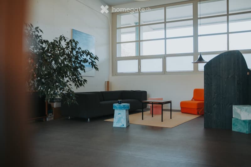 Modern living room with large windows, black sofa, orange chair, small table, and decorative stools.