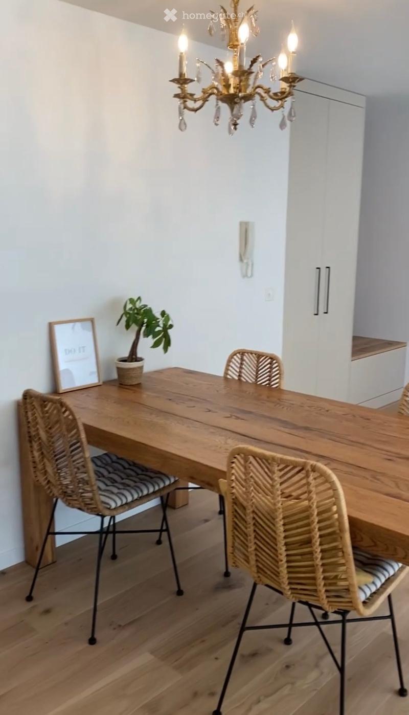Dining area with a wooden table, four wicker chairs, a potted plant, a picture frame, and a chandelier.