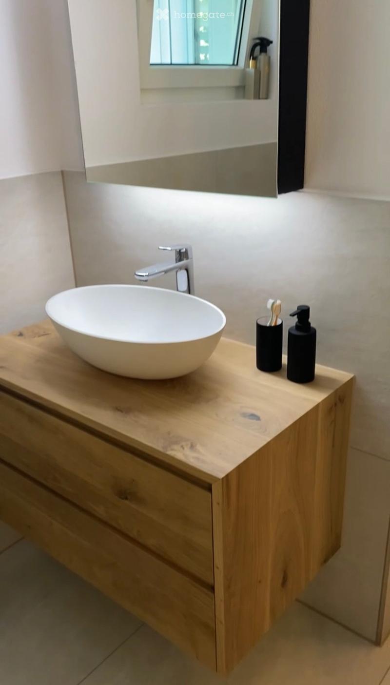Modern bathroom with a wooden vanity, a round sink, a sleek faucet, and a mirror above.