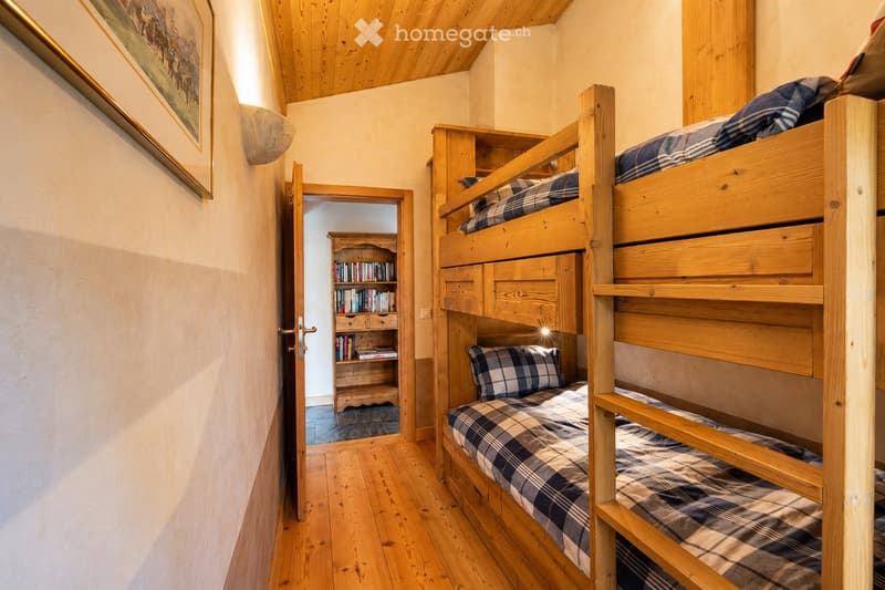Cozy attic bedroom with wooden bunk bed, bookshelf, and picture frame on the wall.