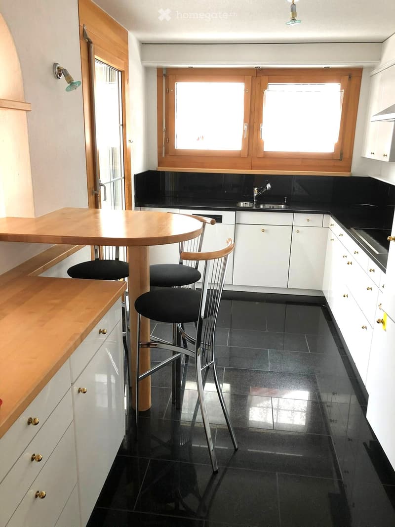 Modern kitchen with white cabinets, black countertops, and a wooden island table with two chairs.