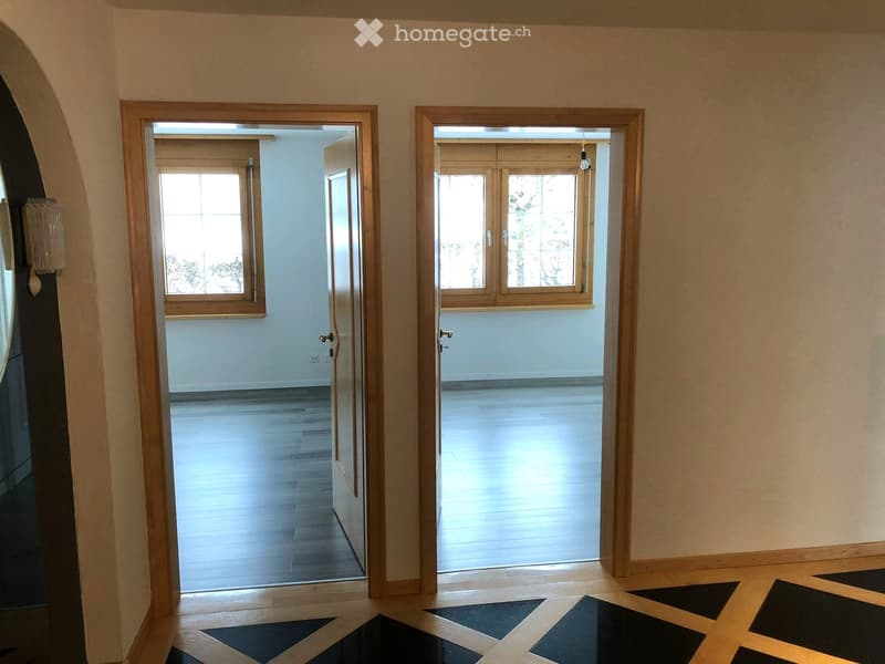 Empty hallway with wooden doors leading to two rooms, light-colored walls, and a patterned floor.