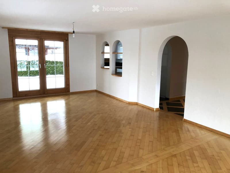 Empty room with polished wooden flooring, white walls, arched doorways, and a large sliding glass door leading to an outdoor area.