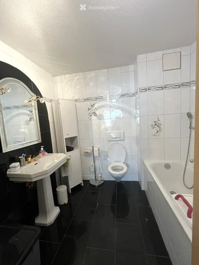 Modern bathroom with black tiles, white fixtures, a large mirror, a sink, a toilet, and a bathtub.