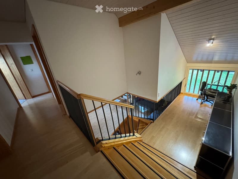 Staircase with wooden railings and a small landing area featuring a desk and chair near a large window.