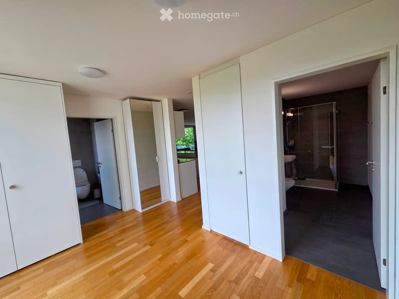 Bright hallway with wooden flooring, white walls, and open doors leading to a bathroom and another room.