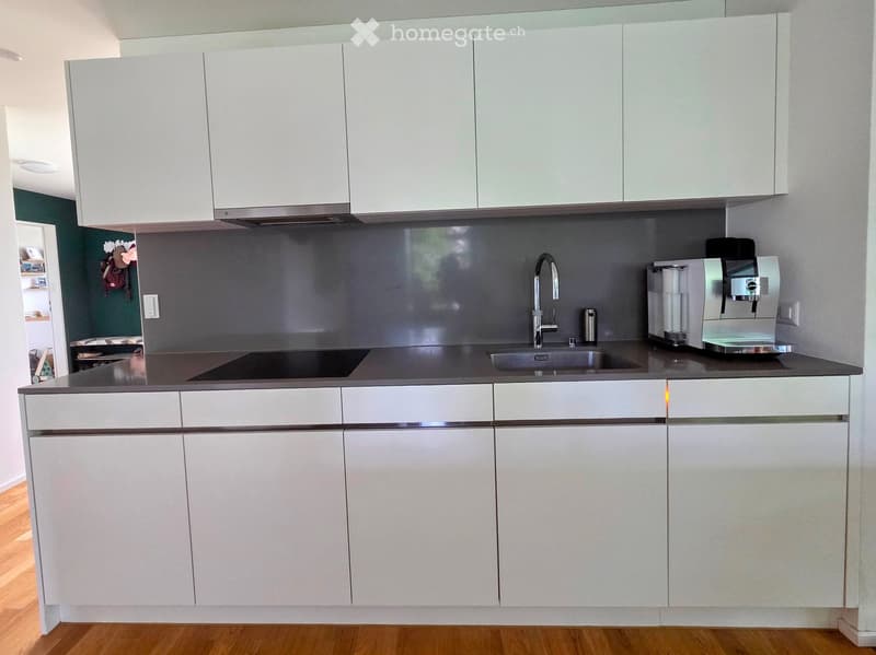 Modern kitchen with white cabinets, stainless steel sink, faucet, and coffee machine on the counter.