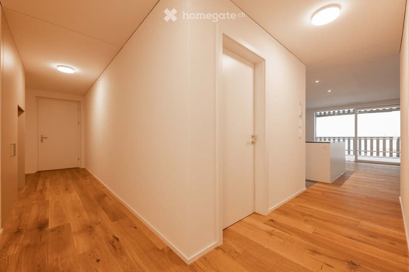 Empty hallway with wooden floors, white walls, two doors, and a balcony with a view