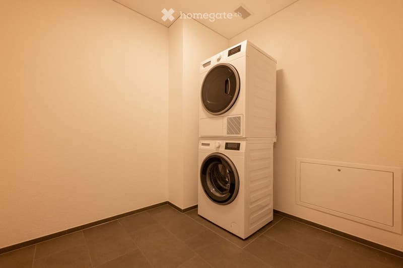 A room with a white stacked washer and dryer, tiled floor, and white walls.