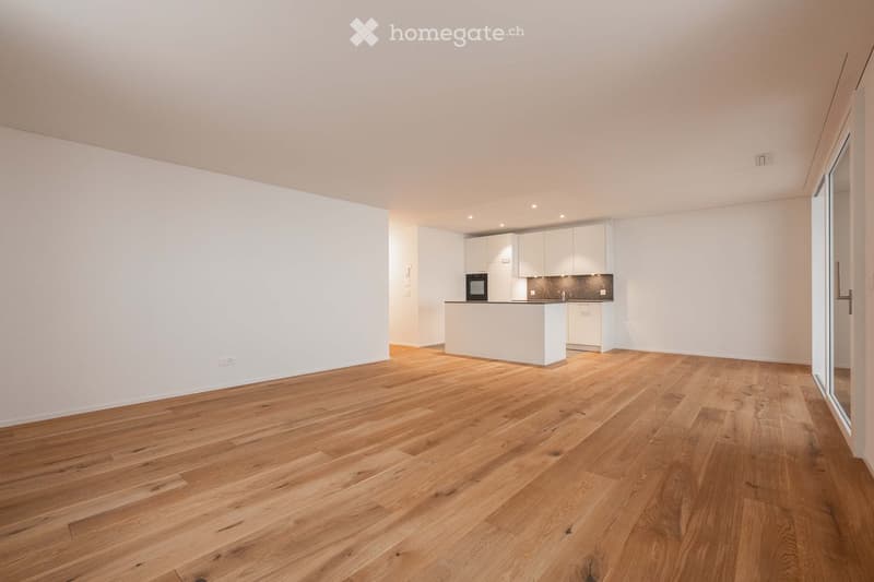 Empty room with white walls, wooden floor, kitchen with island, sliding glass door