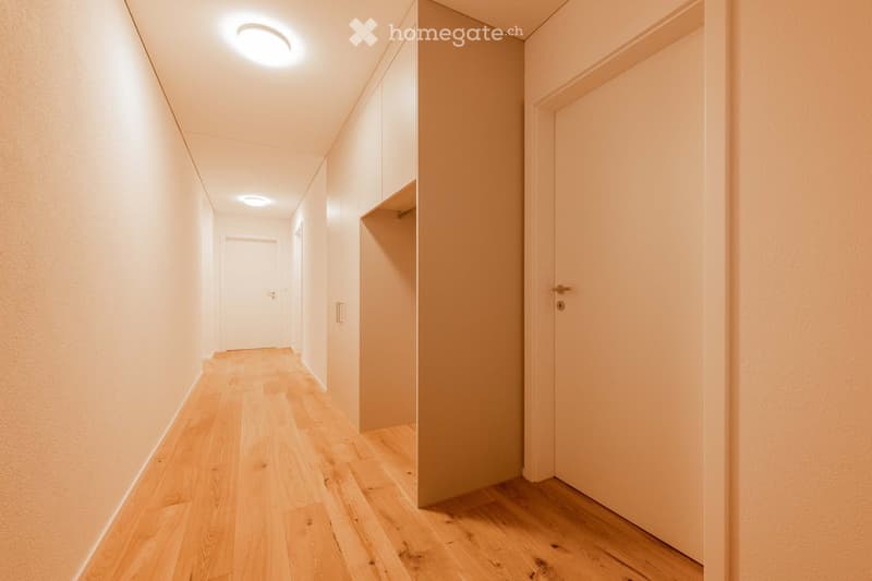 Empty hallway with wooden floor, white walls, recessed lighting, and two doors.