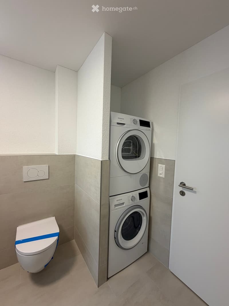 Modern bathroom with a toilet, washing machine, and dryer in a compact space.